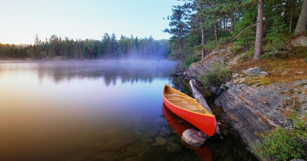 “A lone canoe gliding across a misty lake in Algonquin Provincial Park surrounded by dense forests.”