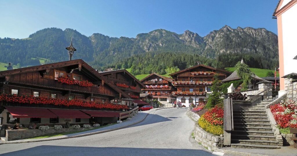 “Traditional wooden chalets in Alpbach, surrounded by green meadows and alpine peaks, under a clear blue sky.”