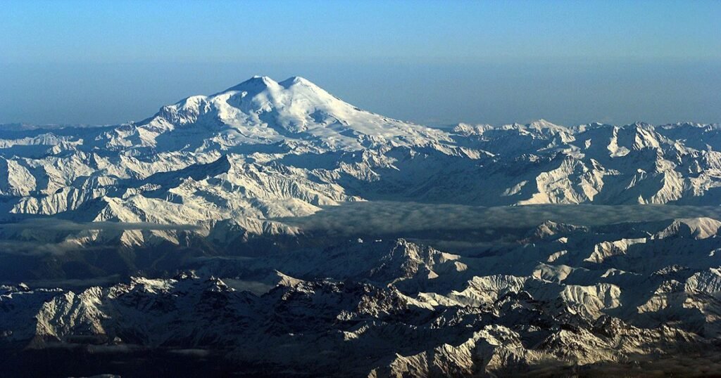 “The towering, snow-covered peak of Mount Elbrus with climbers ascending in the foreground.”