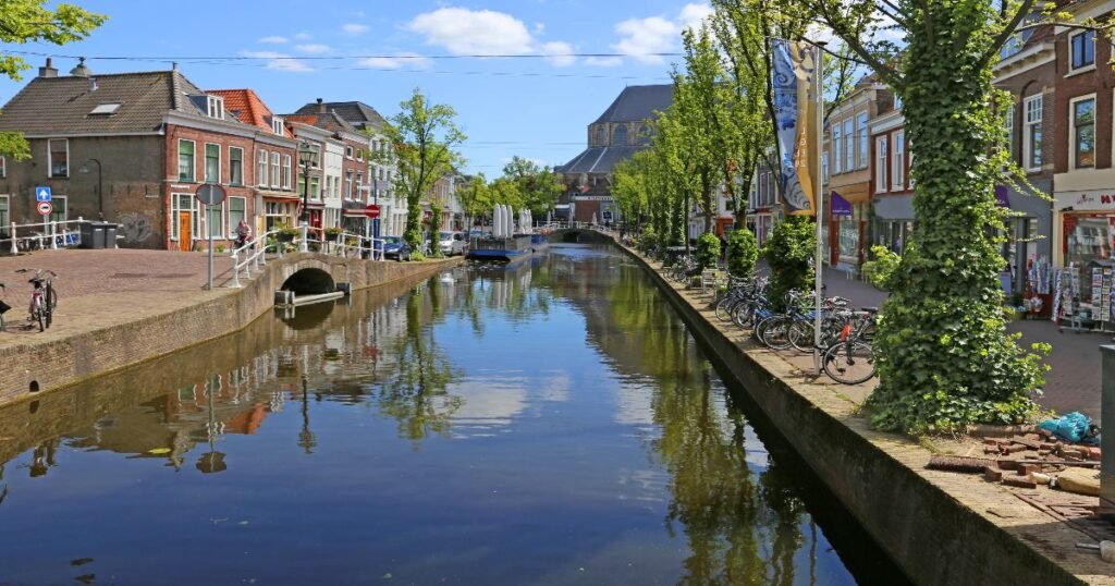  A quiet canal in Delft lined with trees and traditional Dutch buildings, with the New Church tower in the background.