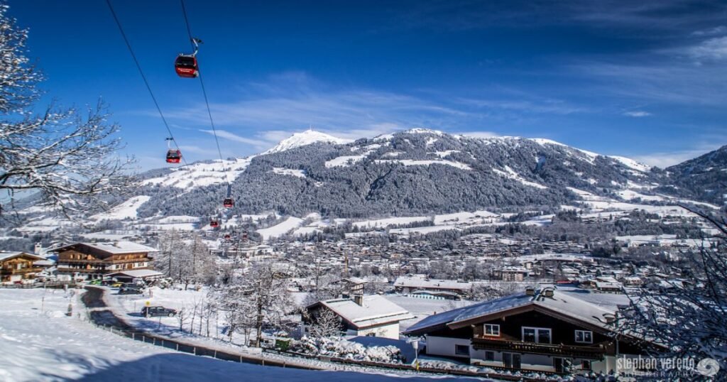 “Picturesque view of Kitzbühel’s ski slopes and town, surrounded by snow-capped peaks and green alpine meadows.”