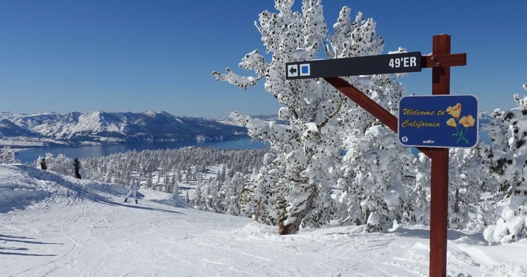 A scenic view of Lake Tahoe surrounded by snow-capped mountains under a bright blue sky. 