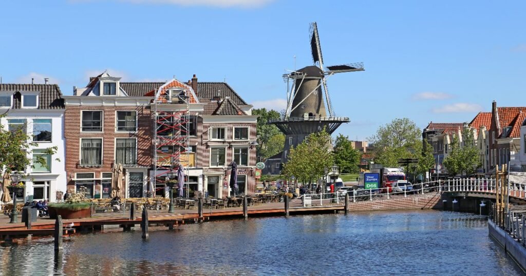 Historic canal-side houses in Leiden with colorful reflections in the calm water on a sunny day.