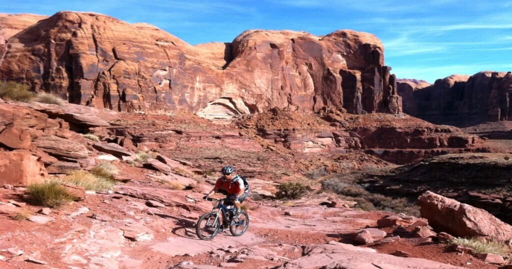 A mountain biker navigating a rocky trail surrounded by red rock formations in Moab.