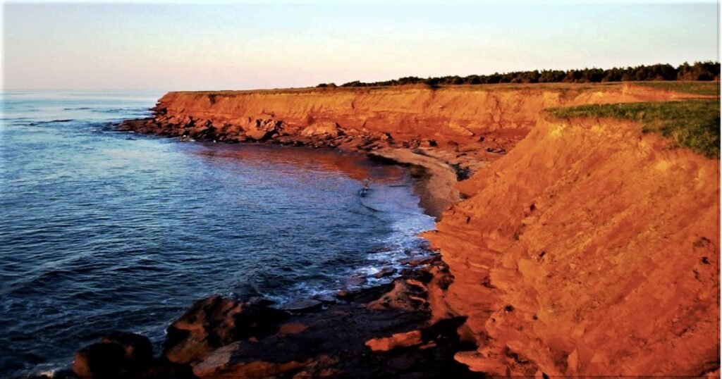 “Red sandstone cliffs along the shoreline of Prince Edward Island National Park, with waves crashing against the beach.”