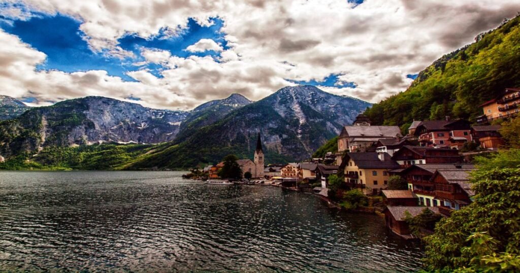 “A kayak gliding over the calm waters of Hallstatt Lake, with traditional wooden houses and snow-capped mountains reflected in the water.”