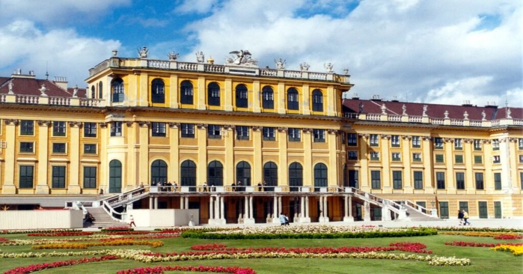 The grand Schönbrunn Palace is surrounded by lush gardens and fountains under a bright blue sky.