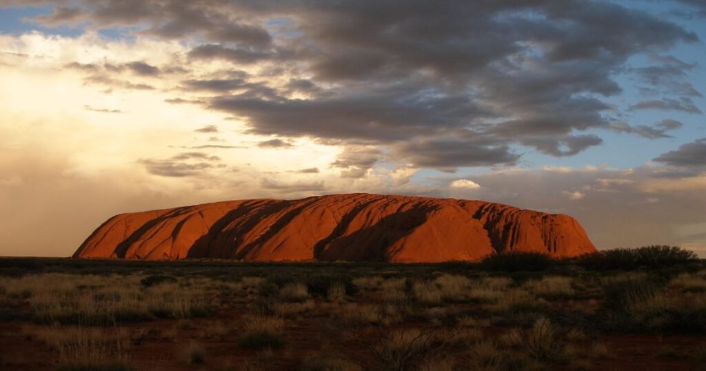  Uluru’s towering red rock formation glowing in the golden hues of sunset in the Australian Outback.