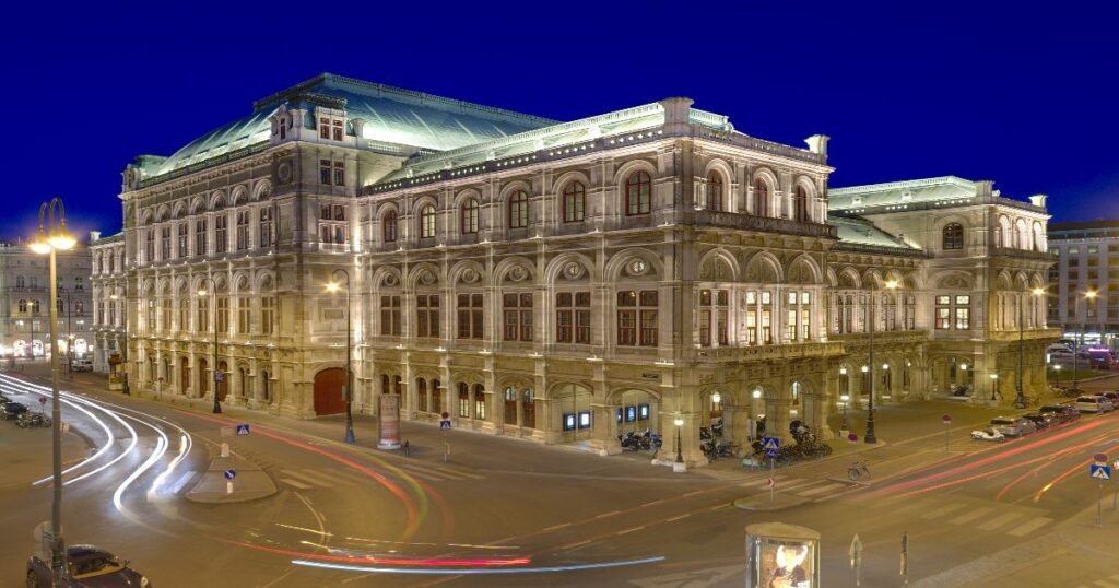 The grand Vienna State Opera building is illuminated at night with elegant classical architecture.