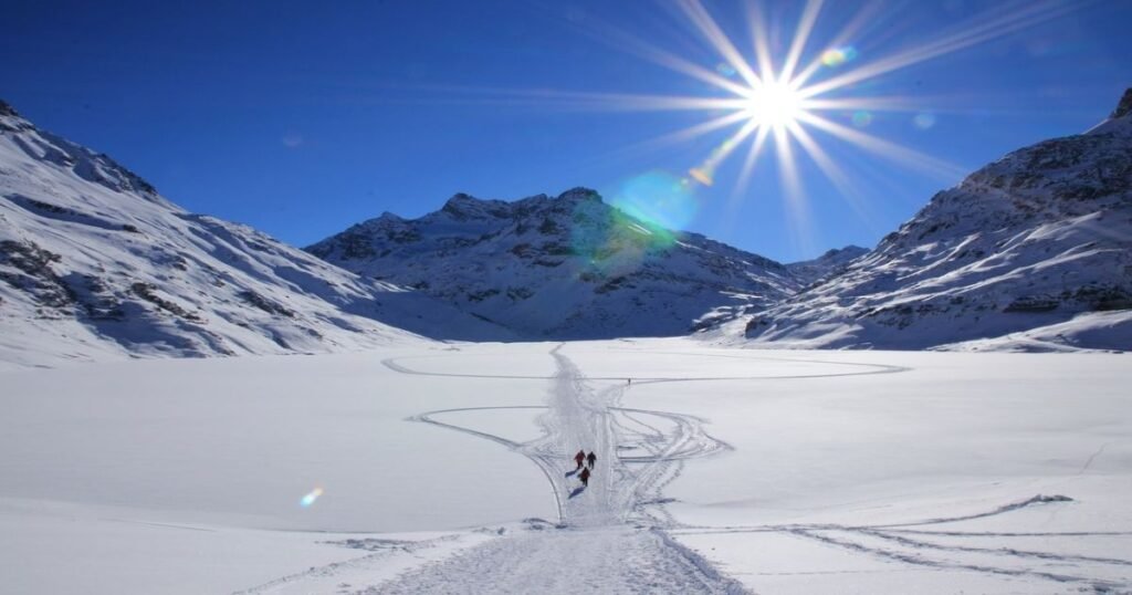 “Snowboarders descending the slopes of Lech Zürs am Arlberg, surrounded by snow-covered mountains and clear blue skies.”
