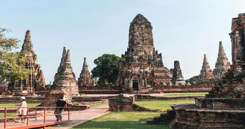 “Ancient ruins of Ayutthaya Historical Park, featuring tall stupas and Buddha statues against a blue sky.”