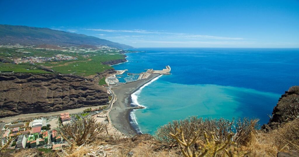 Surfers riding the waves along the stunning black-sand beaches of the Canary Islands with a volcanic backdrop.