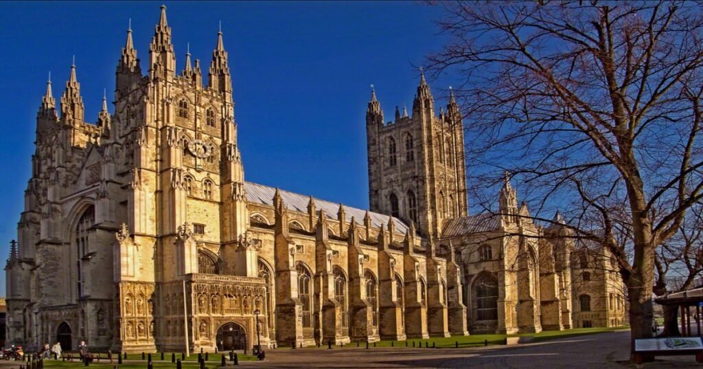 “Canterbury Cathedral’s towering spires and intricately detailed Gothic façade, surrounded by lush green lawns.”