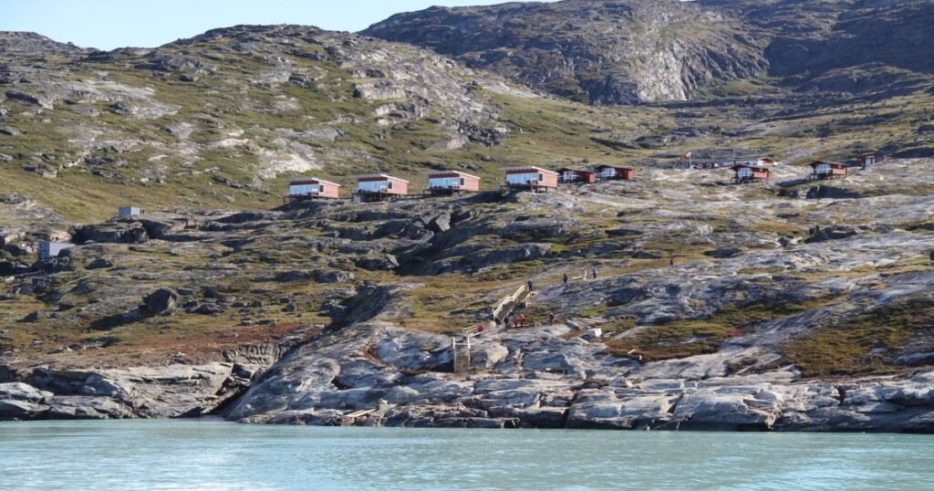 “Eqi Glacier, with towering ice walls reflecting in the calm waters of the fjord, viewed from Glacier Lodge Eqi.”