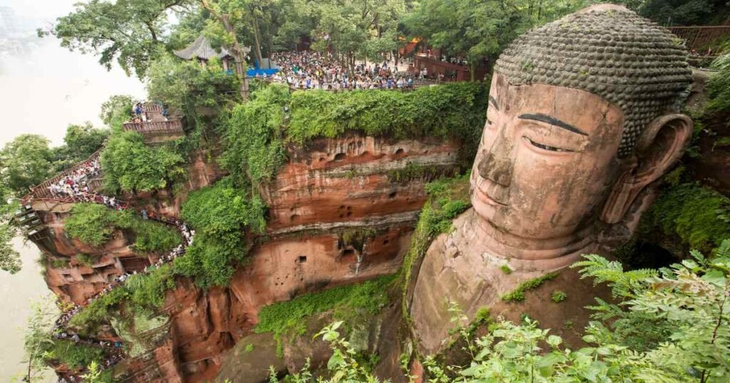 The towering Giant Buddha of Leshan, carved into a cliff, surrounded by lush greenery and rivers below."