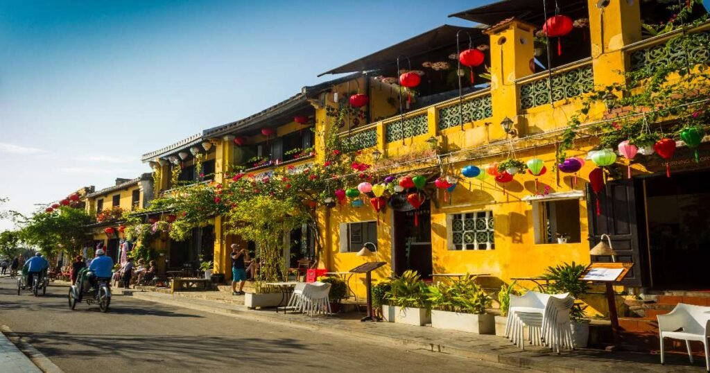 "Streets of Hoi An Ancient Town, lined with yellow buildings and traditional wooden shops with hanging lanterns outside."