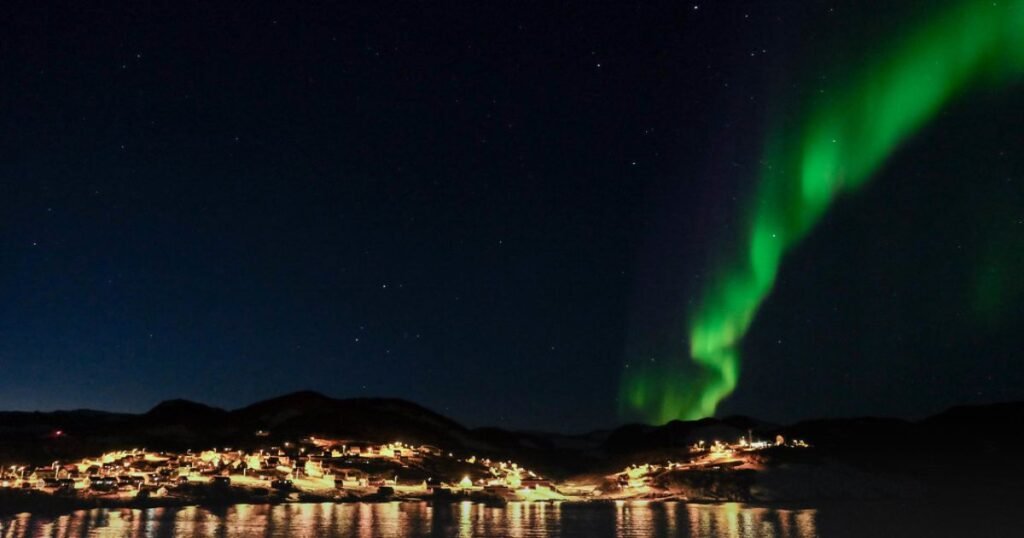 “Ittoqqortoormiit town, glowing in night surrounded by snow-covered peaks and icy fjords.