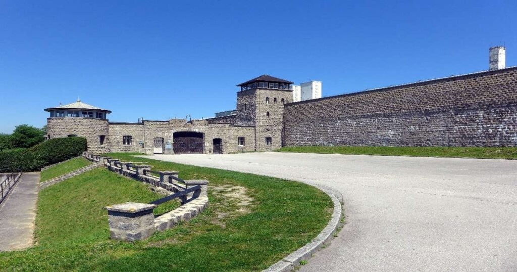 “The solemn grounds of the Mauthausen Memorial, with stark stone walls and a distant sky.”