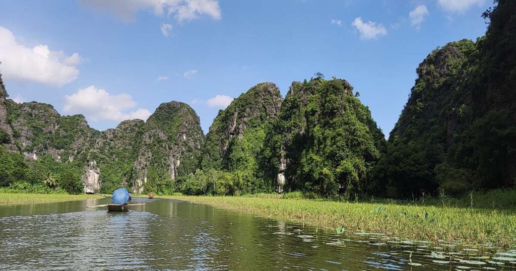 "Tourists taking a boat ride along the Ngo Dong River through towering limestone cliffs in Tam Coc, Vietnam."