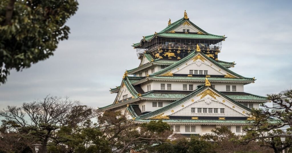 "Osaka Castle standing tall with its golden accents, surrounded by lush greenery"