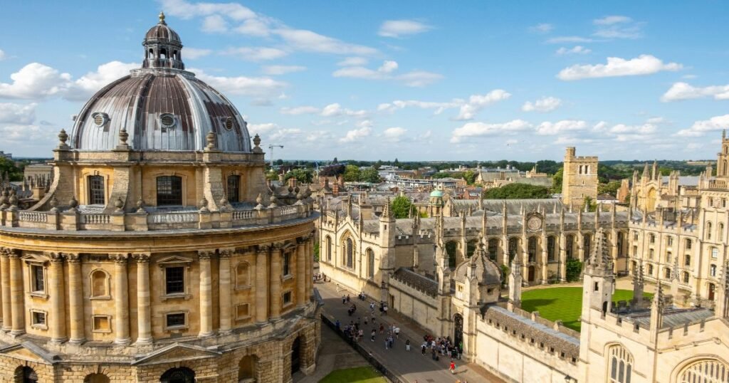 “The Radcliffe Camera, a grand circular building, standing amidst the spires and historic college buildings of Oxford University.”