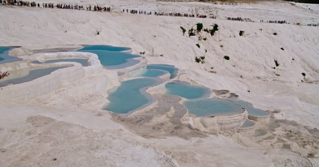 "The white travertine terraces of Pamukkale, with turquoise thermal pools set against a blue sky."