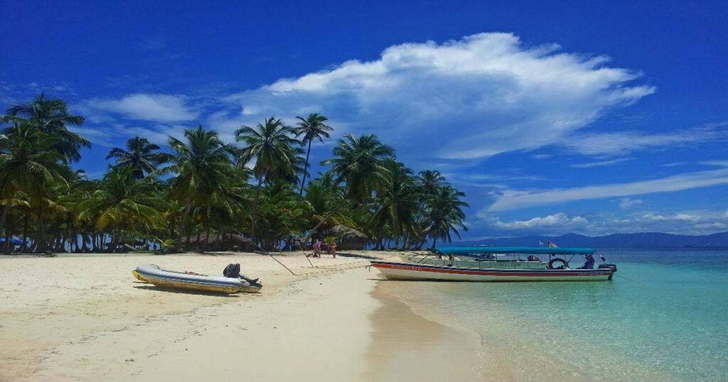 “Pristine white-sand beach of the San Blas Islands, with turquoise waters and a Guna Yala community in the background.”