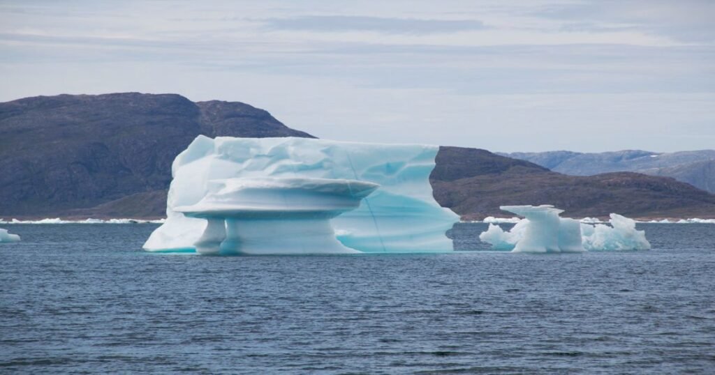 “Blue icebergs floating in the calm waters of a South Greenland fjord.