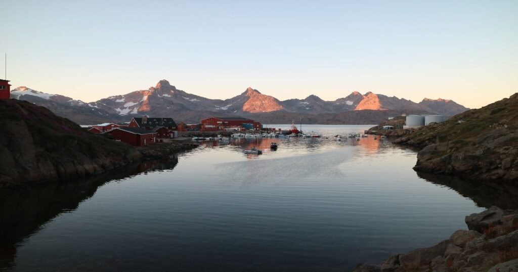 “Tasiilaq town surrounded by towering snow-covered mountains and the icy waters of Ammassalik Fjord.”