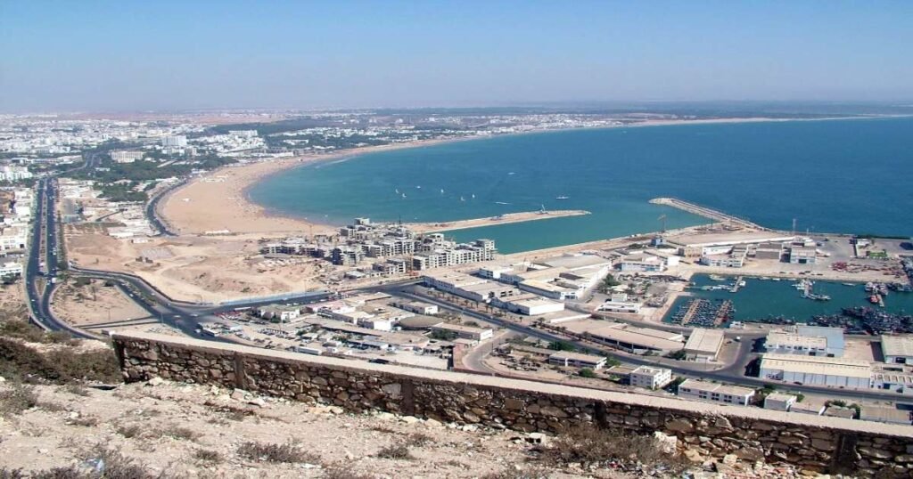  "Golden sands and turquoise waters at Agadir beach with palm trees and a modern marina."