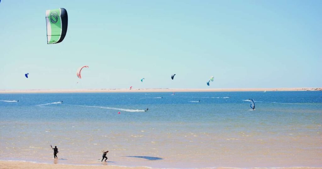 “Kitesurfers gliding over the turquoise waters of Dakhla Lagoon with desert sand dunes in the background.”