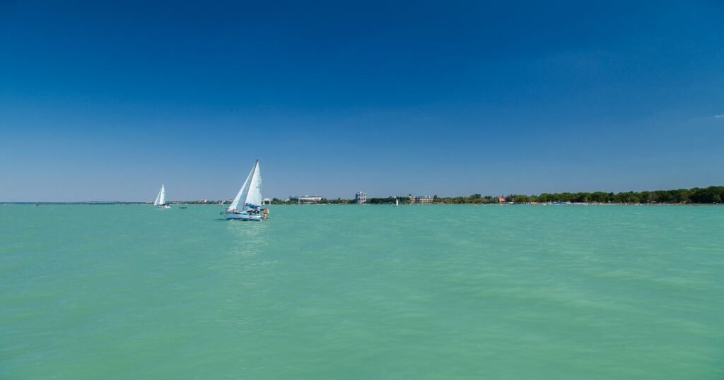 “Wind surfers and sailors gliding over the turquoise waters of Lake Balaton on a sunny day.”