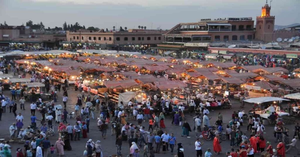  "A bustling scene in Jemaa el-Fnaa Square with market stalls, performers, and the Koutoubia Mosque in the background."