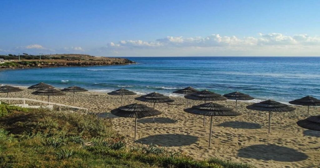 "Nissi Beach's white sand and turquoise waters with sunbathers and parasols under a sunny sky."