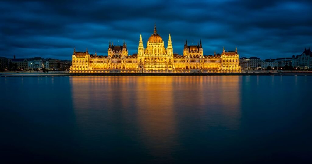 Iconic Hungarian Parliament Building illuminated at night along the Danube River with ornate Gothic Revival architecture.