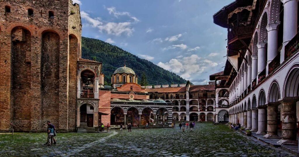 "The vibrant frescoed facade of Rila Monastery with snow-capped mountains behind."