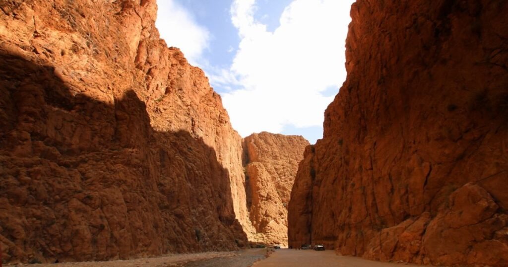 "Majestic red cliffs of Todra Gorge rising above a riverbed with a blue sky overhead."