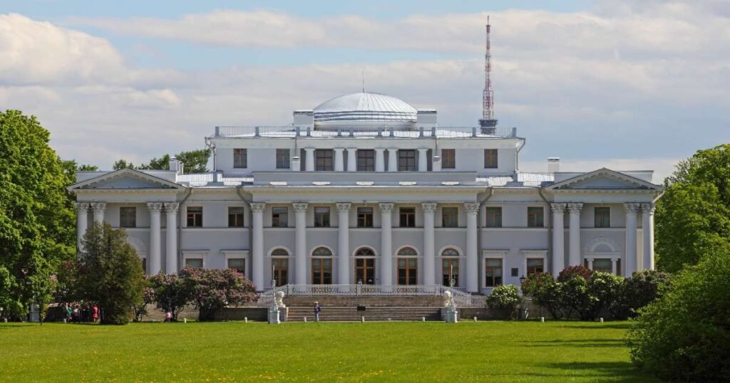 “Neo-classical facade of Yelagin Palace, surrounded by the greenery of Yelagin Park on a sunny day.”