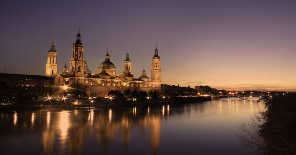 Basilica of Our Lady of the Pillar illuminated at night with reflections in the Ebro River.