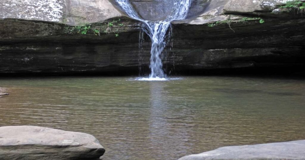 The serene Cedar Falls surrounded by mossy rocks and greenery in Hocking Hills State Park.