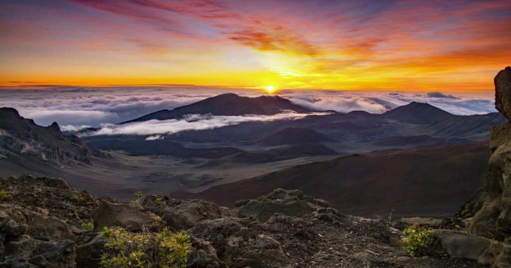 Haleakalā’s summit at sunrise with colorful skies and clouds below.