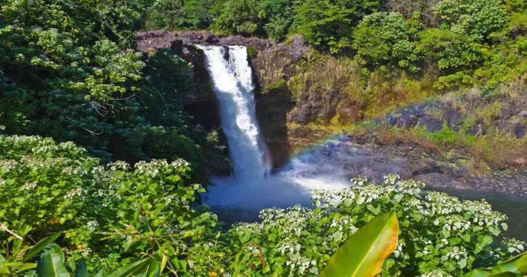 Rainbow Falls surrounded by lush tropical greenery under a blue sky