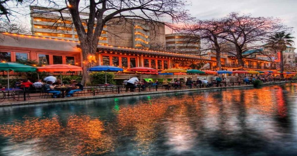 A scenic view of the San Antonio River Walk with colorful umbrellas lining the water.