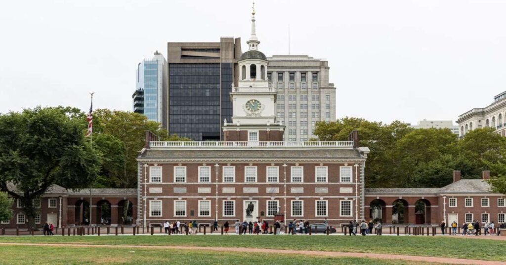 Independence Hall with a blue sky and American flags waving in front.